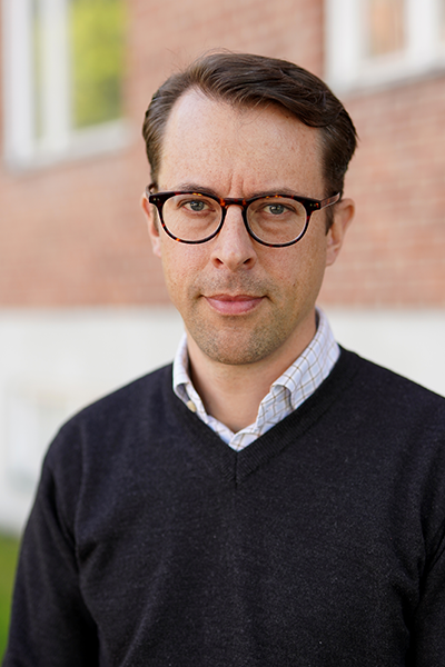 Man with dark hair and glasses looks into camera. Portrait photo. 