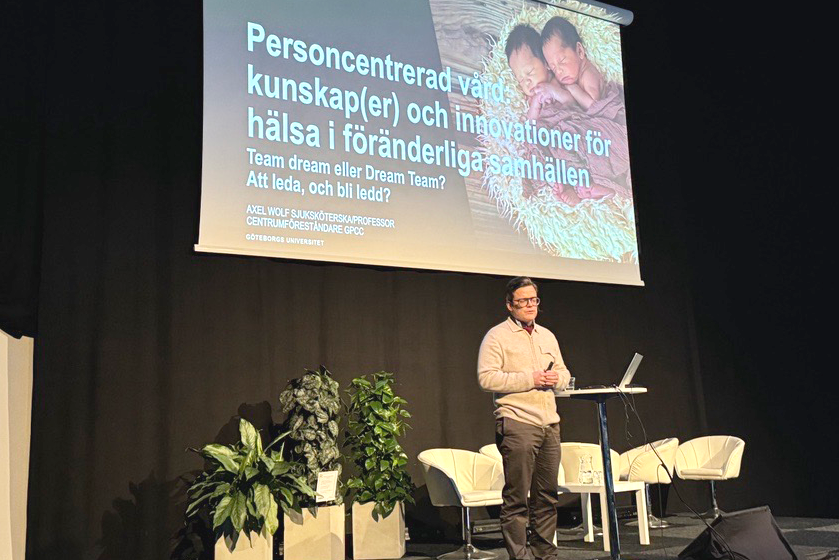 A man standing on stage, presenting in front of a screen. Image.