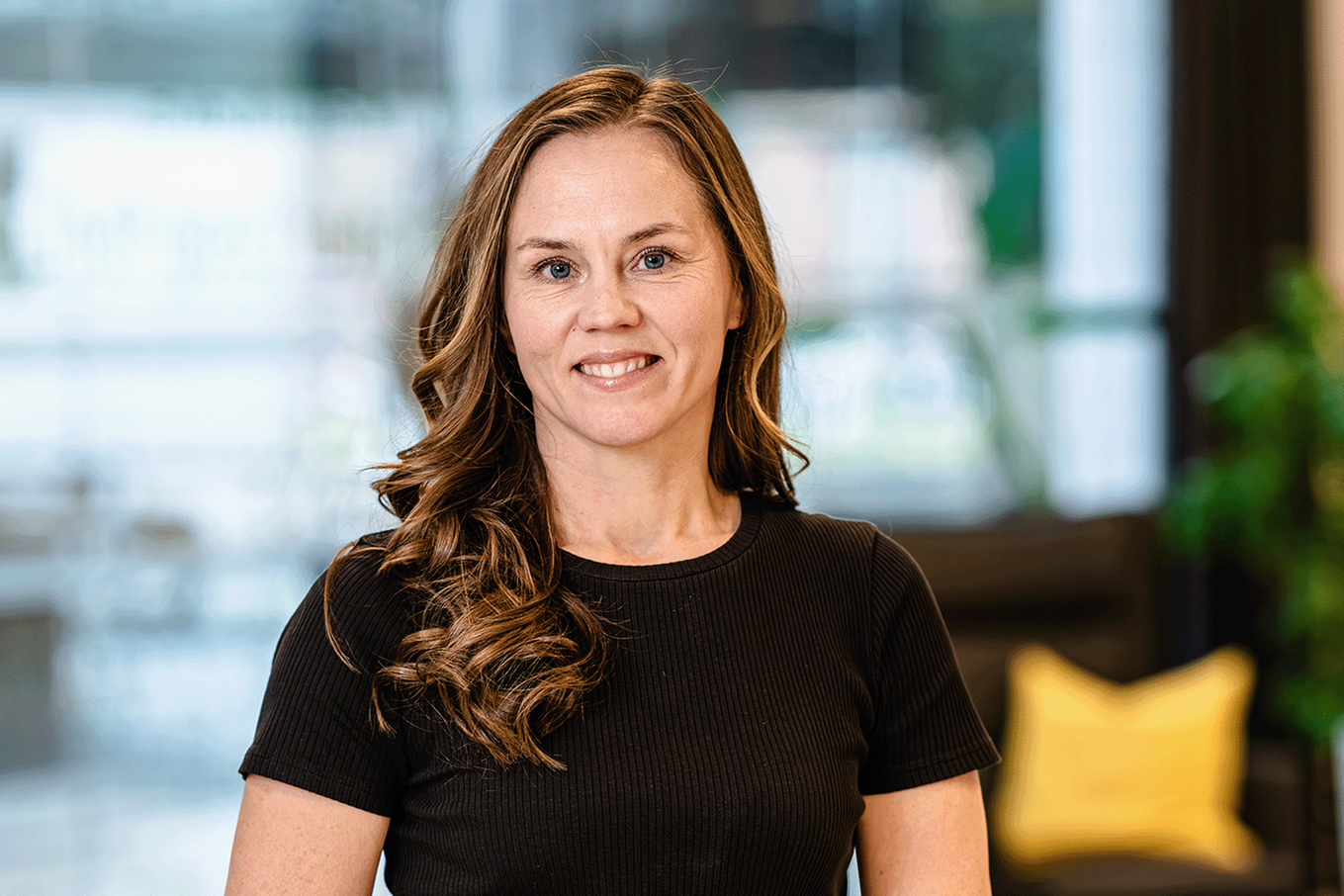 Kvinna med långt hår och svart tröja tittar in i kameran och ler. Bild.